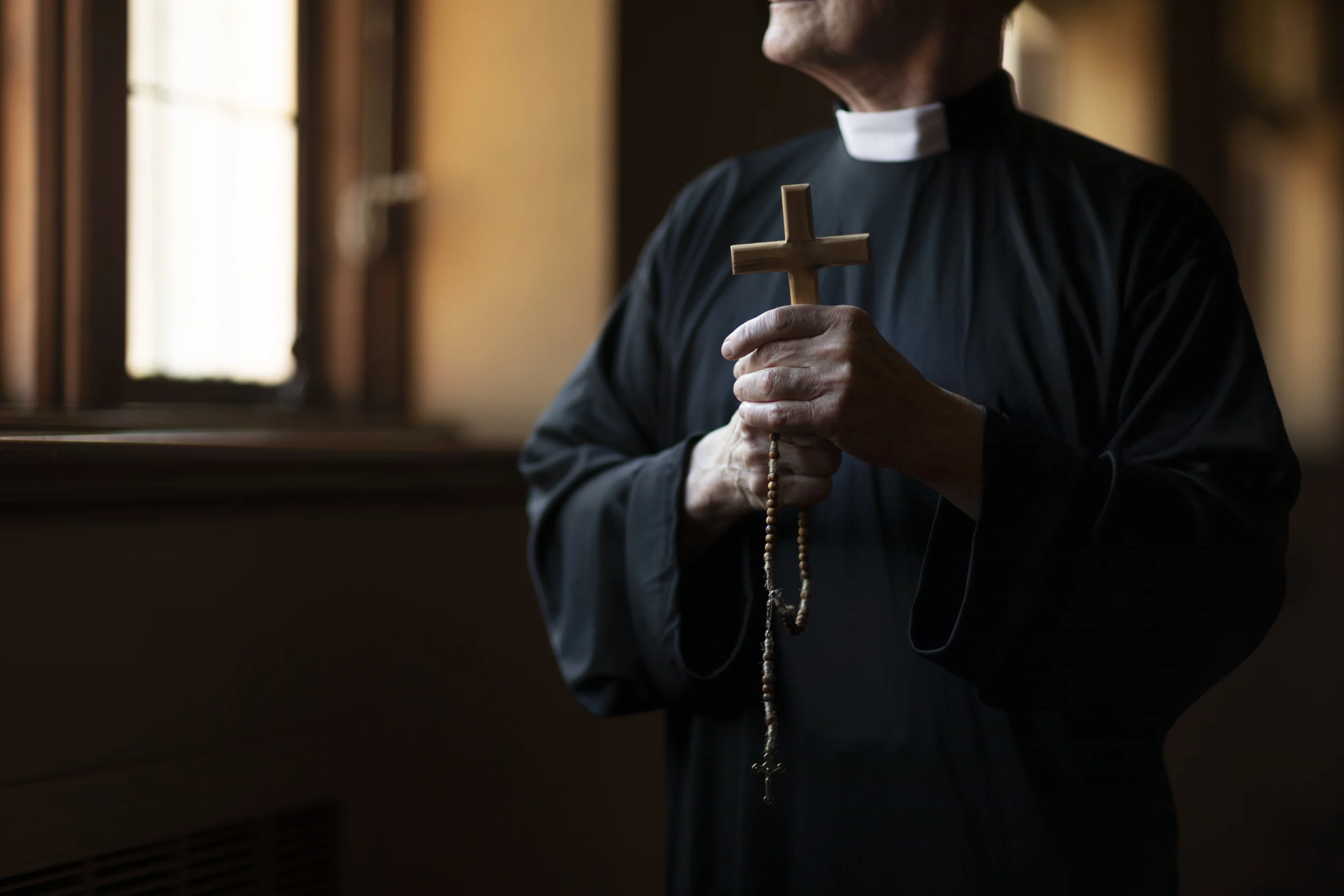 sacerdote sostiene cruz y rosario con la mano